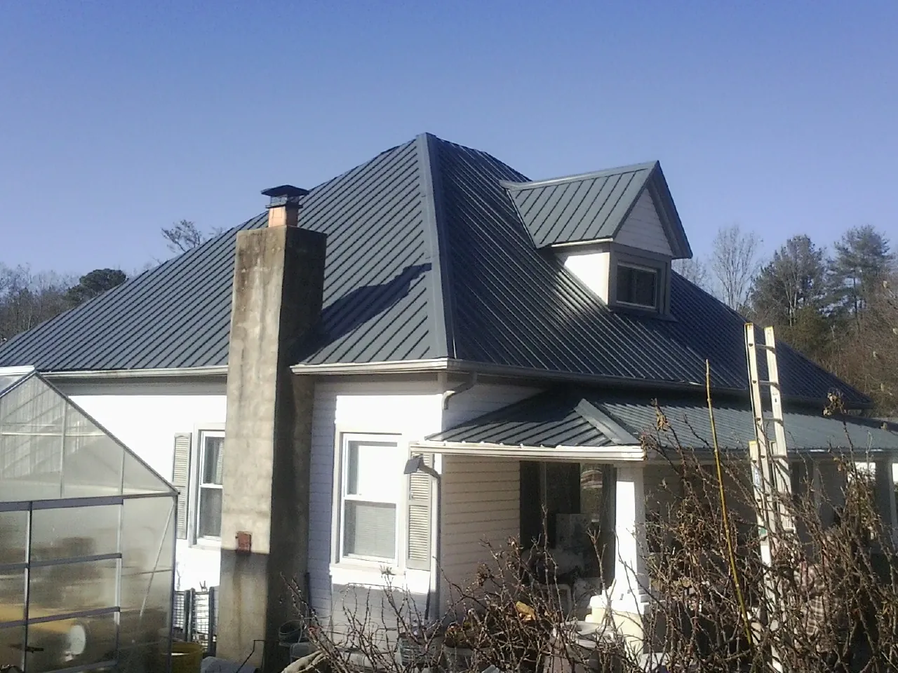 Dark blue standing seam metal roof on a white farmhouse with dormer — Slate & Tile Roof Repair by Roofing Brothers in Saunderstown