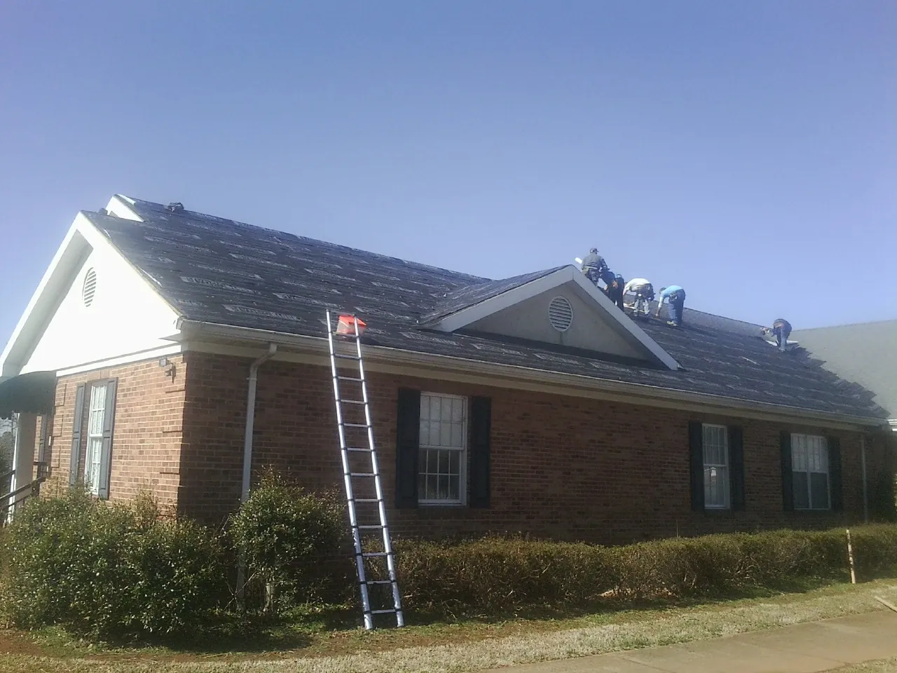 Crew tearing shingles off a brick ranch roof with a ladder set — Emergency Roof Repair work by our crew in Saunderstown