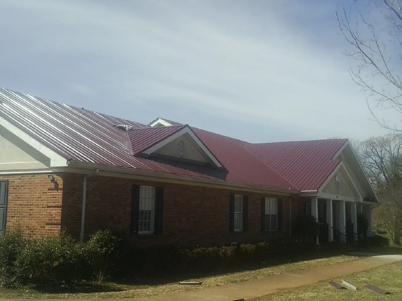 Red metal roof with gabled entries on a long brick building, from a Hail Damage Roof Repair job in Saunderstown