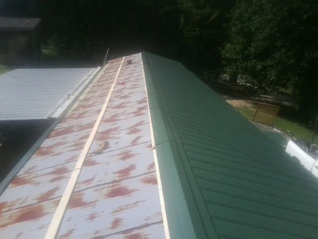 Old rusted panels beside newly installed green metal roofing — Wind Damage Roof Repair by Roofing Brothers in Saunderstown
