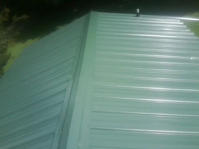 New green metal panels meeting at the ridge of a roof — Flat Roof Repair work by our crew in Saunderstown