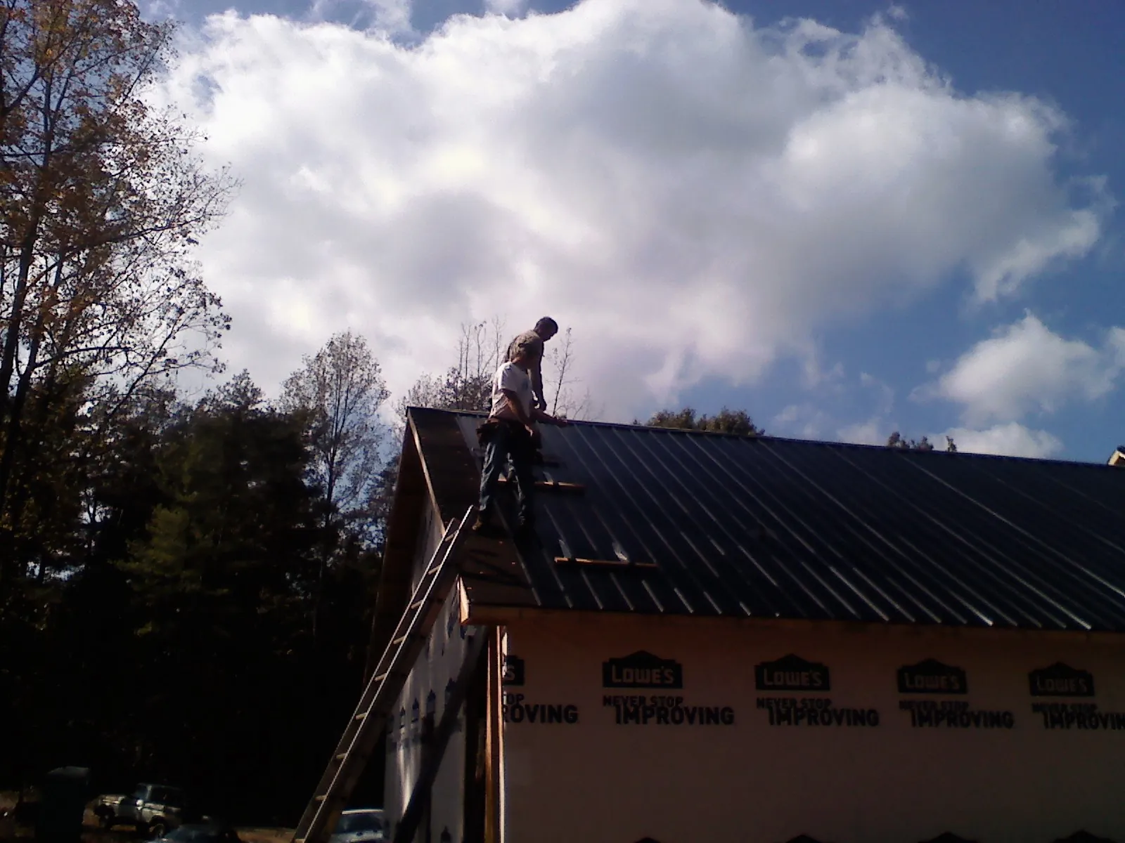 Roofer fastening dark metal panels high against a cloudy sky, from a Roof Inspection job in Saunderstown