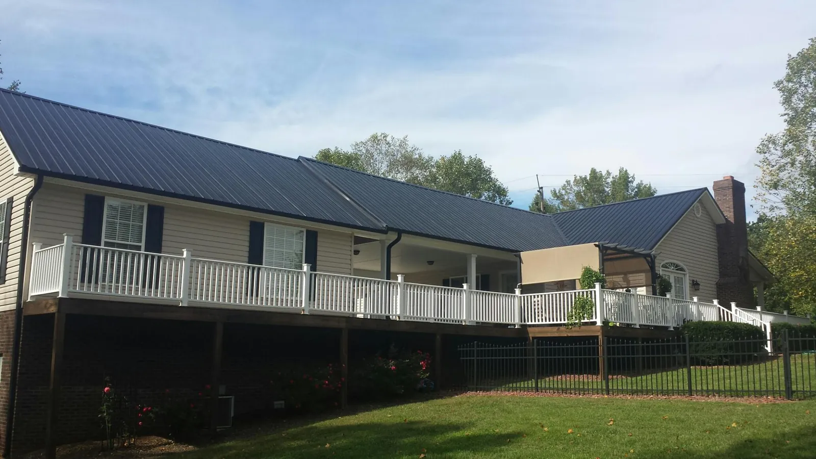 Black metal roof above a long white railed deck on a hillside home in Saunderstown