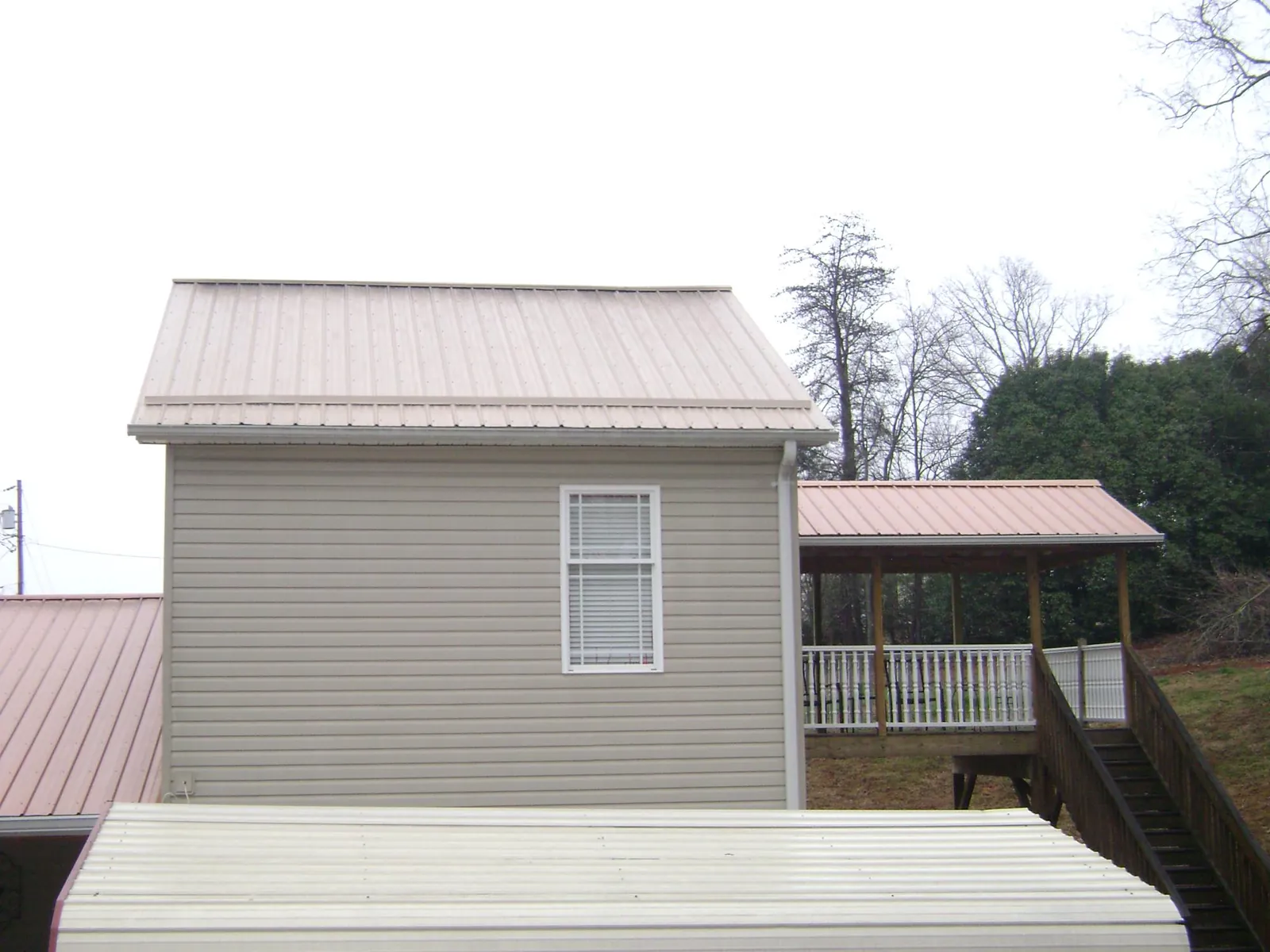 Tan metal roofs on a two story addition and attached porch, from a Roof Replacement job in Saunderstown